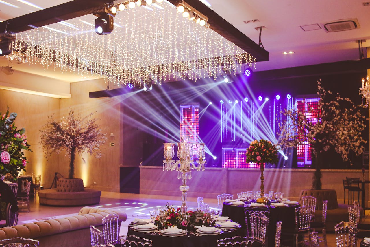 services-02 Stunning ballroom setup decorated with crystal chandeliers, floral arrangements, and vibrant stage lighting.