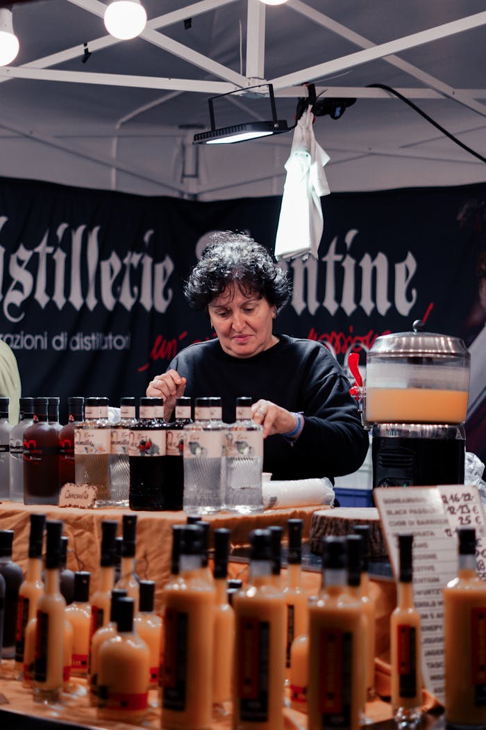 A woman organizing a variety of bottles at an indoor market stall with a retail display.